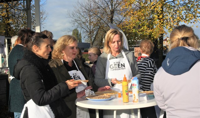 Teamleden van De Tweemaster delen zelfgebakken pannenkoeken uit.