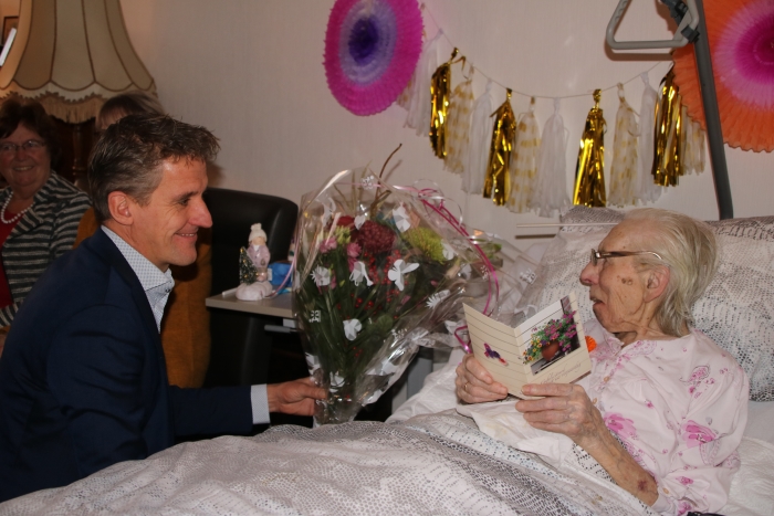 Mevrouw Meerkerk ontvangt bloemen van de bestuurder van De Lange Wei omdat zij 100 jaar is geworden