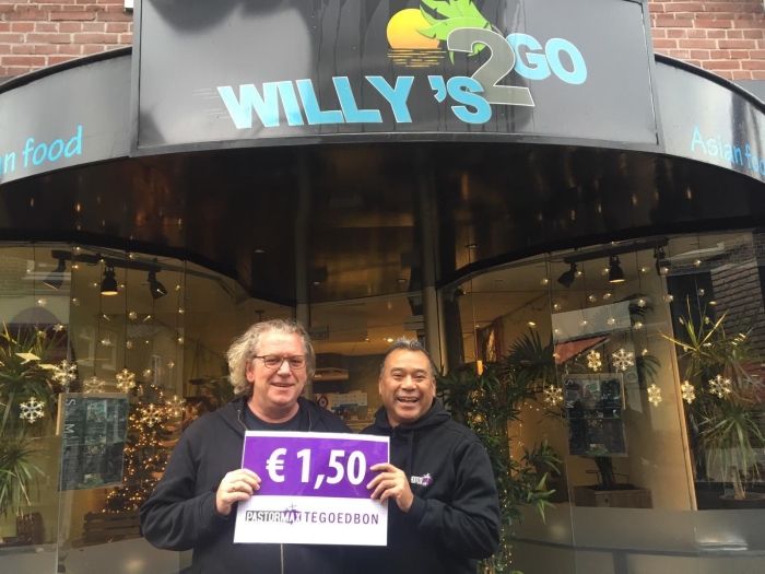 Pastor Max (links) samen met Willy Titalepta (rechts) voor de winkel in Ede waar de stokjes saté uitgedeeld zullen worden. Centraal het 'heb je wat' kaartje waar aandacht voor wordt gevraagd.
