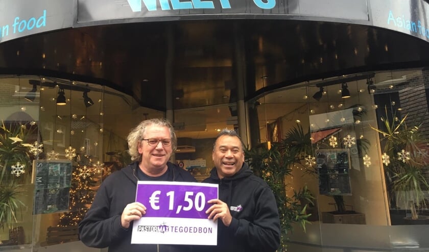 Pastor Max (links) samen met Willy Titalepta (rechts) voor de winkel in Ede waar de stokjes saté uitgedeeld zullen worden. Centraal het 'heb je wat' kaartje waar aandacht voor wordt gevraagd.