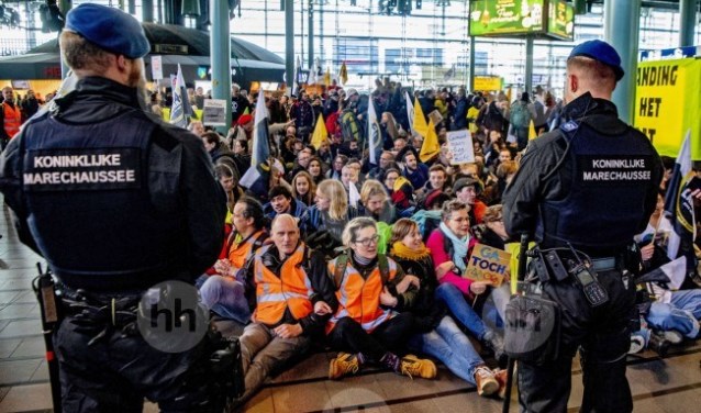 Een grote groep actievoerders zit nog gearmd in de hal omringd door marechaussees.