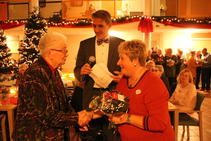 Eén van de jubilerende vrijwilligers van De Lange Wei ontvangt een bloemetje van vrijwilligerscoordinator Francis 't Hooft. Op de achtergrond: Bestuurder Sander van IJsseldijk