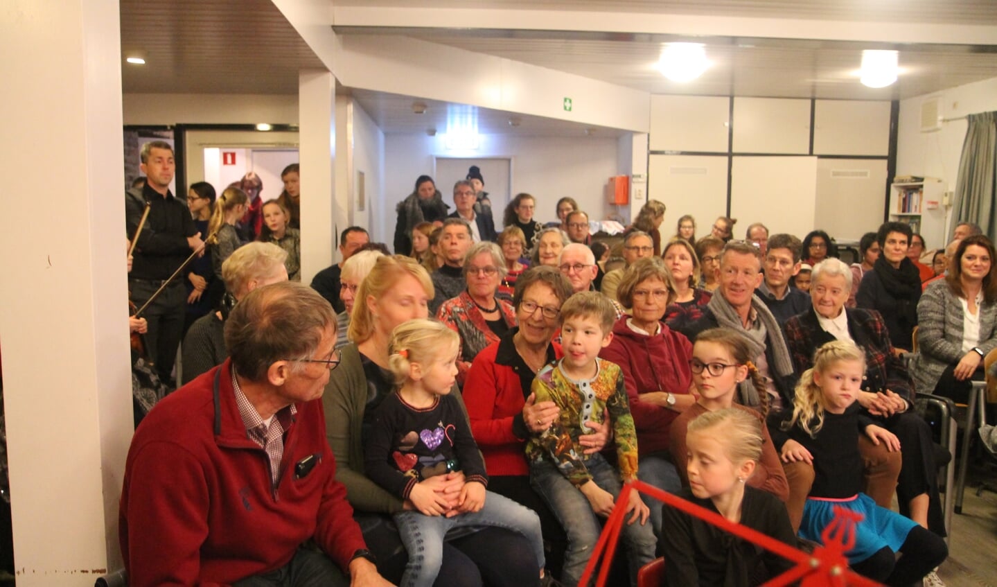 een overvolle zaal met publiek tot in de hal