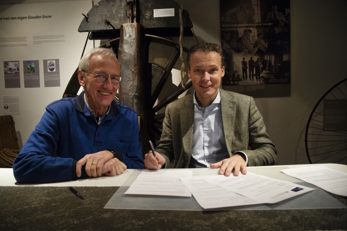 Jan Langman, directeur Touwfabriek Langman (rechts en Jan Cozijnsen, voorzitter Stichting Oud Nijkerk (links), ondertekenen het vernieuwde sponsorcontract. Op de achtergrond het grote wiel van de touwslagerij.