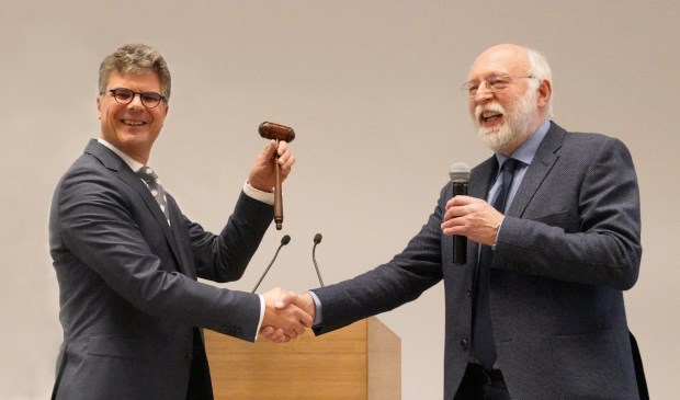 Hans Oosters (links) ontvangt de voorzittershamer uit handen van vicevoorzitter Kees de Kruijf