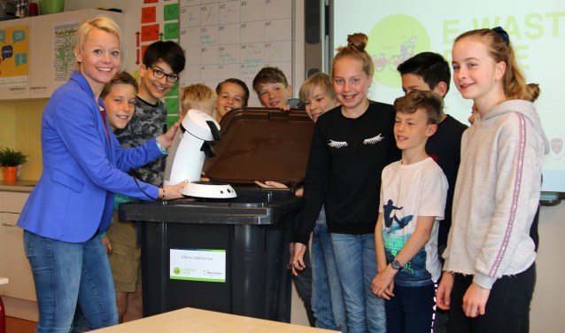 Wethouder Gordon en leerlingen doen een oud koffiezetapparaat in een container.