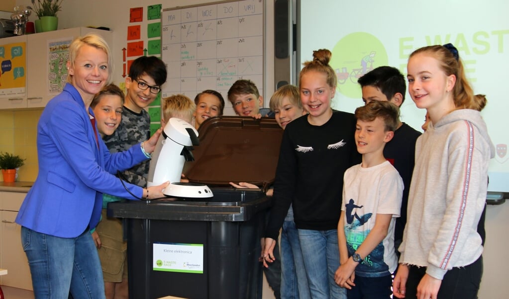 Wethouder Gordon en leerlingen doen een oud koffiezetapparaat in een container.