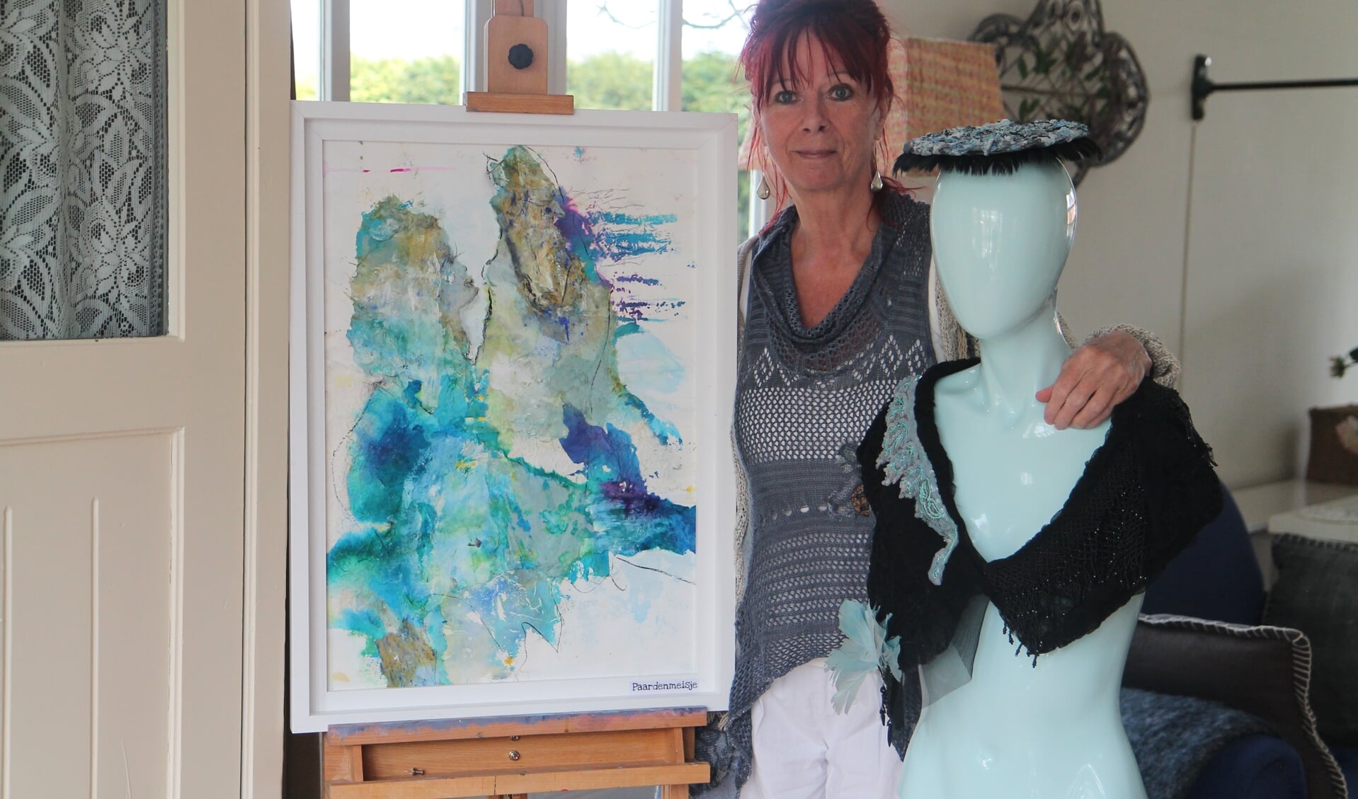 Nelleke Droog met één van haar schilderijen en een paspop met kraag en hoedje.