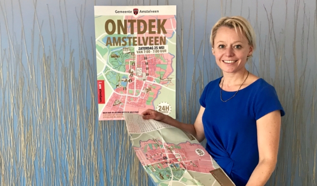 <p>Wethouder Floor Gordon bij de poster van de eerste editie van 24H Amstelveen. Het 24 uur durende programma krijgt in september een tweede editie.</p>