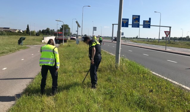 Agenten doorzoeken de berm op zoek naar eventueel weggegooide goederen.