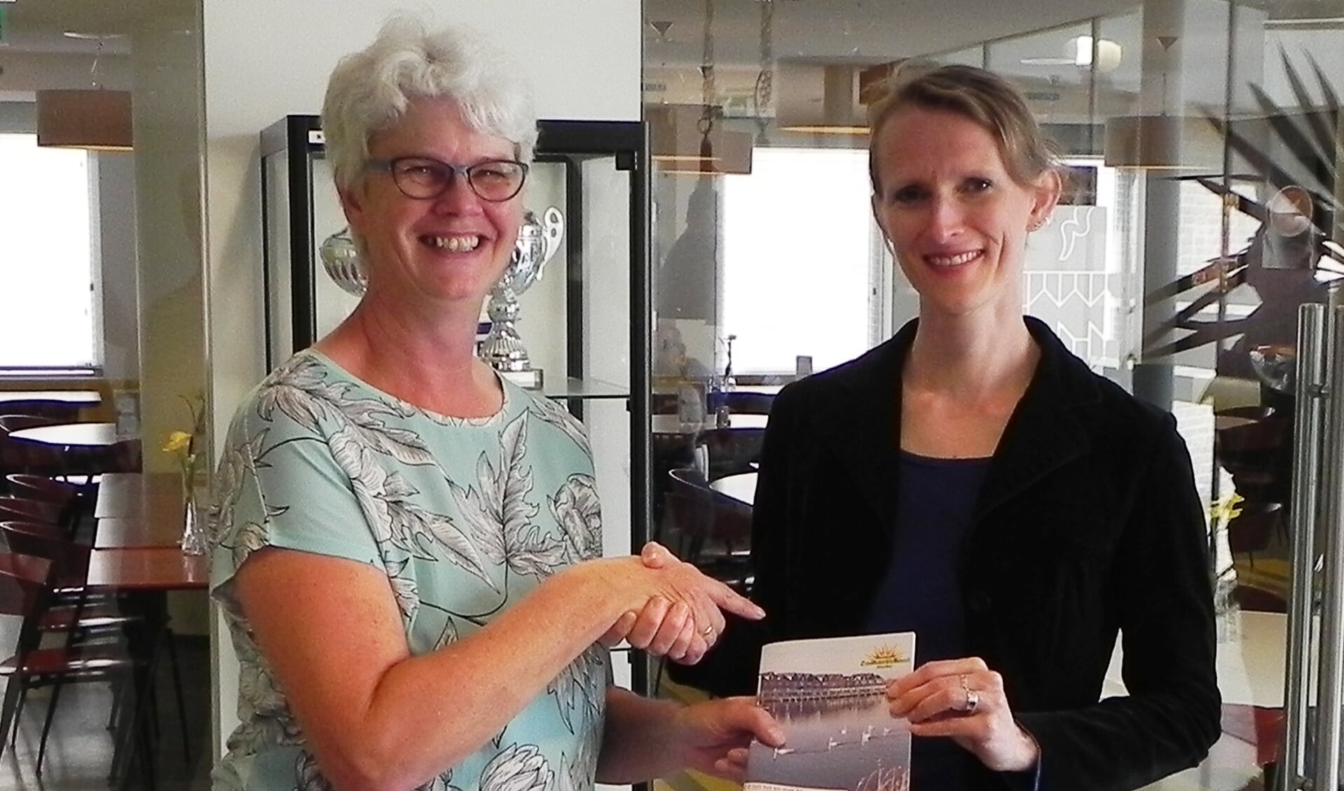 Wethouder Jana Smith-Visser ontvangt het programmaboekje uit handen van voorzitter Annemieke Hoogenhout.