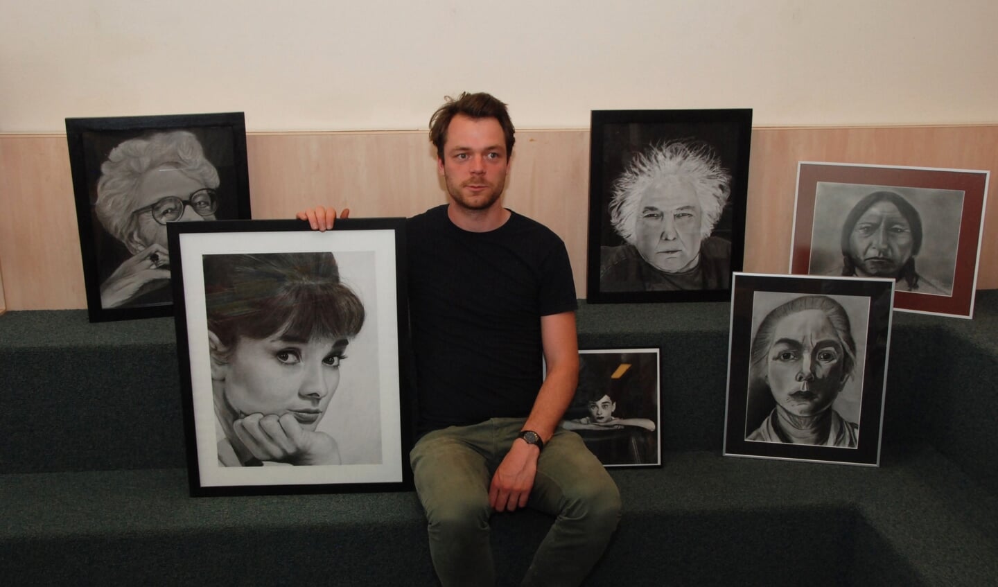 Martijn Versteeg met het portret van Audrey Hepburn en werk van cursisten.