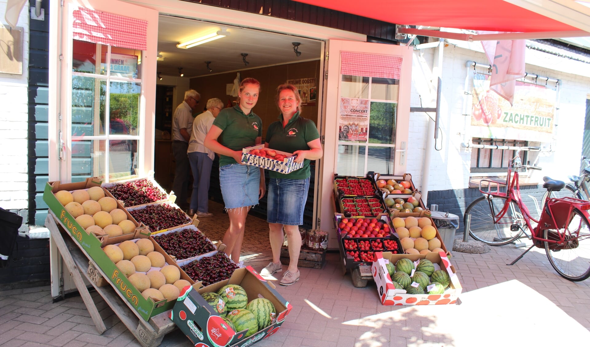 Janny en Mari-An van de Fruithut tussen het zomerse fruit, dat de Woudennbergse winkel momenteel volop in de aanbeiding heeft.