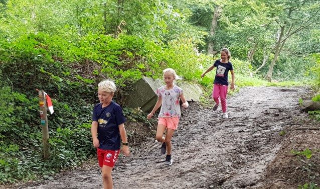 Kinderen glibberen over de helling tijdens de Mud Vally Kids obstaclerun van 2018.