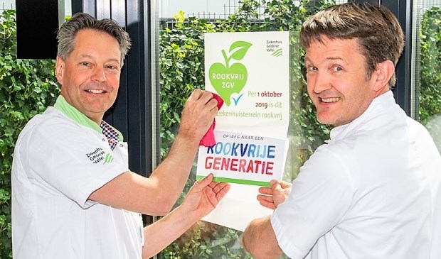 Cardioloog Maurits van der Veen en longarts Jeroen Verheul plakken aankondiging van rookvrij ziekenhuisterrein op rookplek.