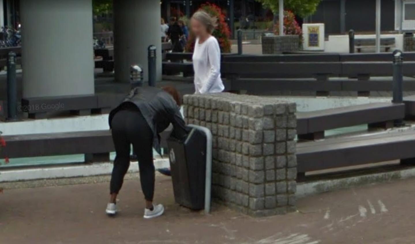 Vlak voor het gemeentehuis rommelt een vrouw wat in een prullenbak.  