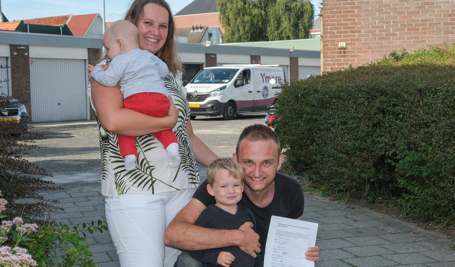 Het gezin Van Diel, met Robert die de handtekeningenactie toont. Op de achtergrond een van de busjes van Ymere die volgens hem de buurt gevaarlijk maken.