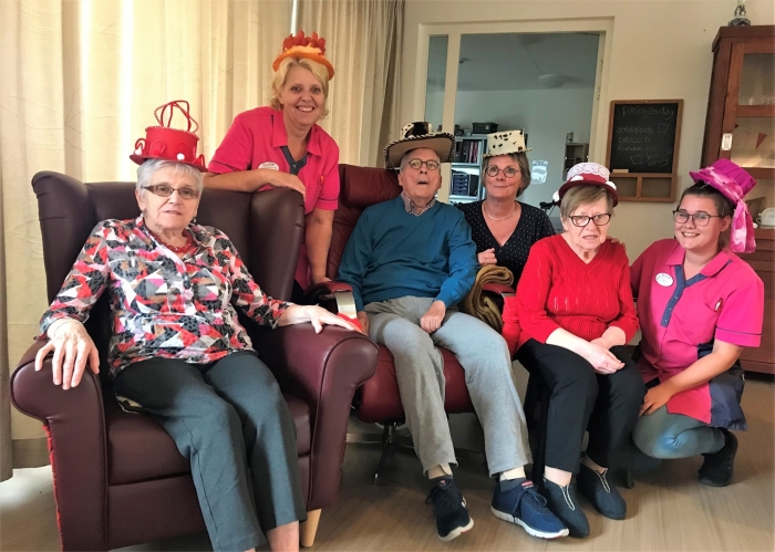 Bewoners van een afdeling kleinschalig wonen poseren met hoed samen met Bea Stooker en een mantelzorger.