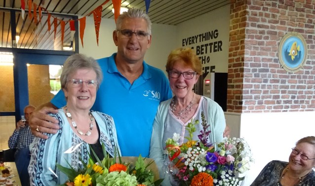De twee jubilarissen Lijda Oudenes en Alij Grammé omarmt door Silvester Claassen