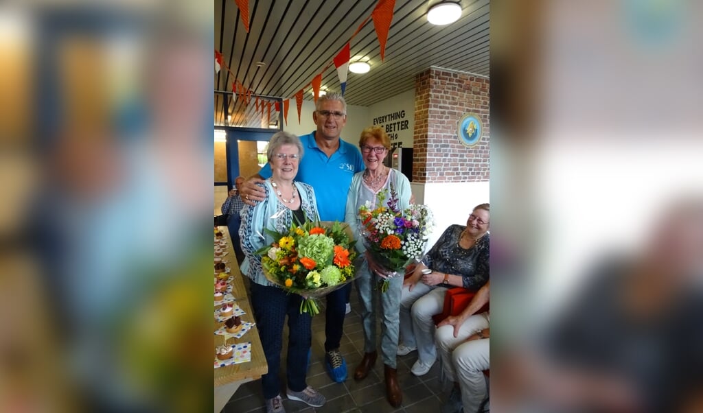 De twee jubilarissen Lijda Oudenes en Alij Grammé omarmt door Silvester Claassen