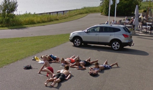 Een groep jongens ligt op het asfalt langs de Tooelnburgerplas.