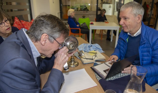 Cees Broekhof bekijkt een zilveren kandelaar met behulp van een loep