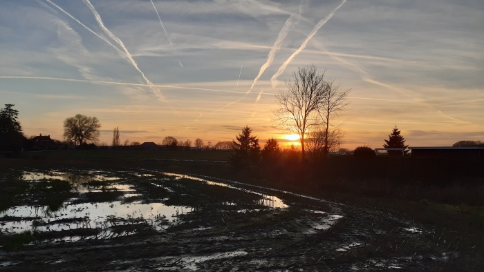 allerlei elementen bij elkaar: vliegtuigstrepen, lucht, land, water en een mooie zonsondergang