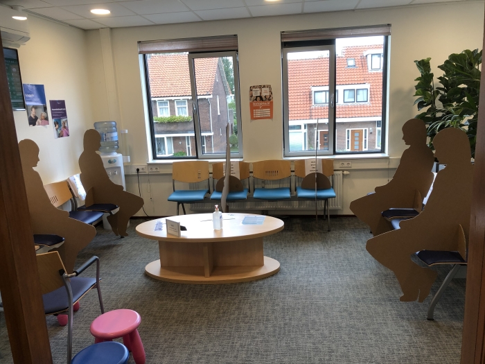Kartonnen poppen in de wachtkamer van Huisartsenpraktijk Amstelwijck. Die zijn geplaatst om ervoor te zorgen dat bezoekers niet dicht bij elkaar kunnen zitten.