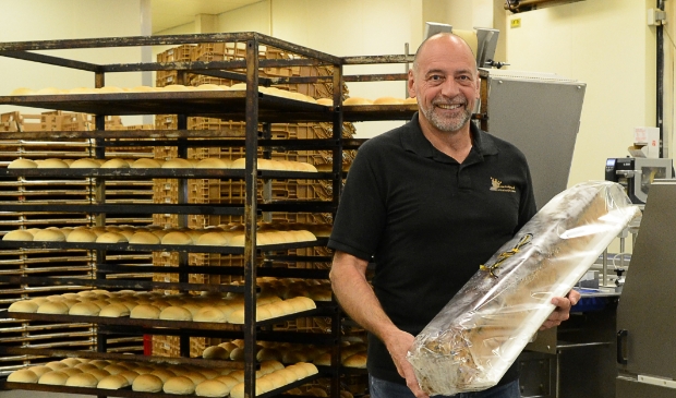 <p>Harrie van Looijengoed met een meter krentenbrood in de ambachtelijke bakkerij.</p>