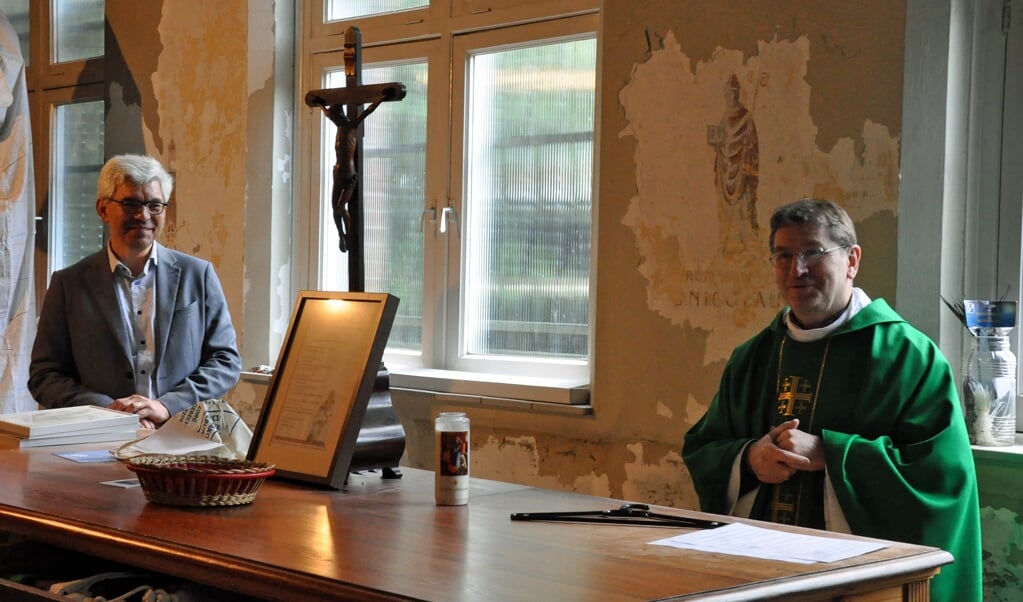 Carel Jansen (links) en pastoor Joachim Skiba zijn blij verrast door de muurschildering van de heilige Nicolaas die zichtbaar wordt.