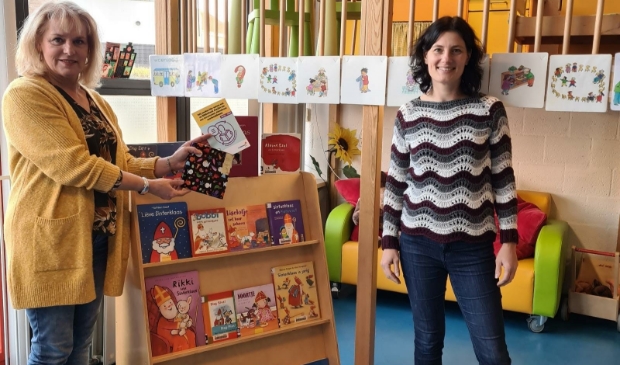 Ellen van Eijmeren (Bibliotheek AanZet) en Leny de Bruin (Wasko Kinderopvang) met het keurmerk Boekstart bij de nieuwe boekenkast waarbij de boekjes goed zichtbaar en op ooghoogte staan.