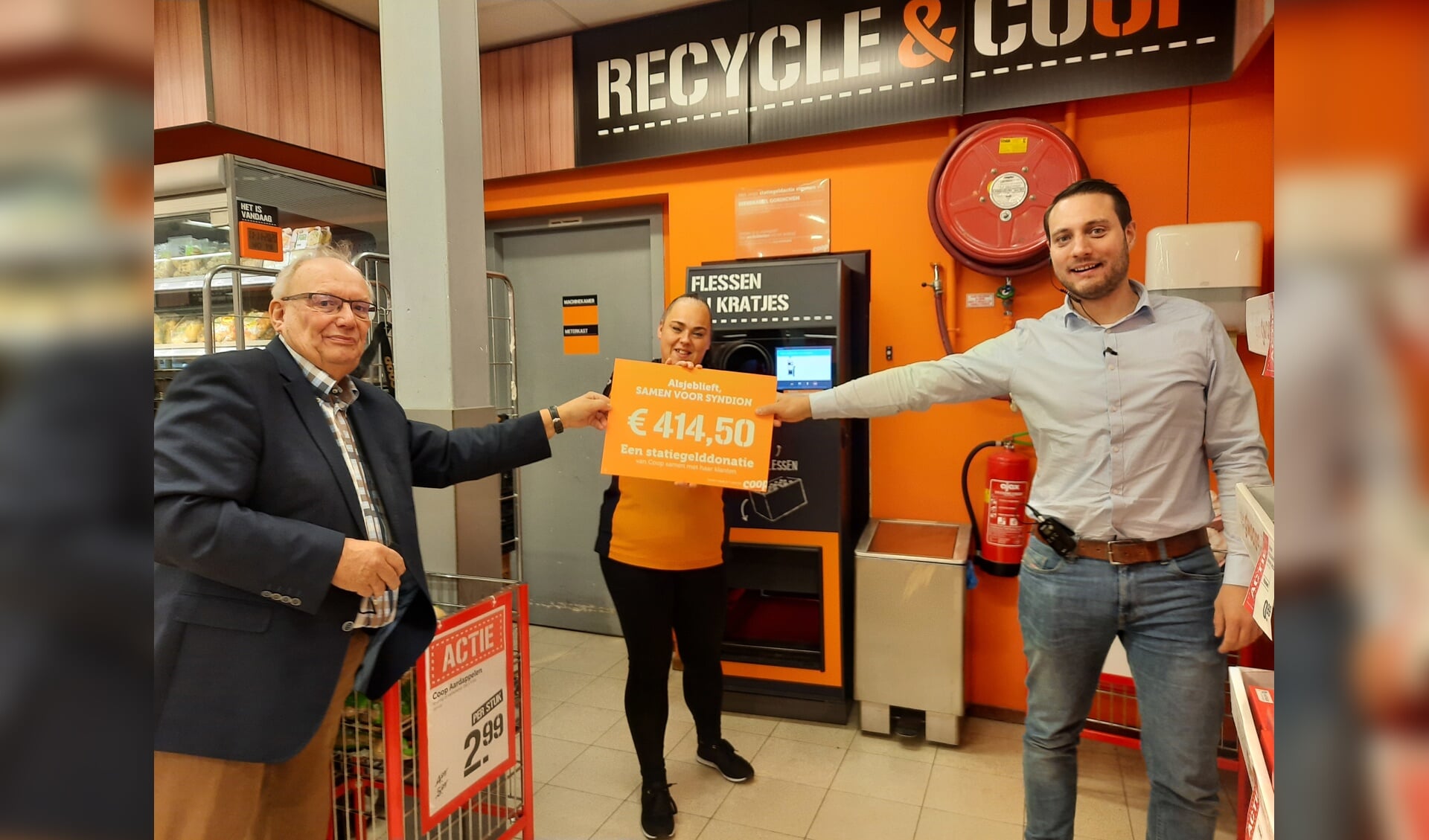 Bart Bruggeman, voorzitter van Samen voor Syndion (links) neemt onder toezicht oog van Daisy, client bij Syndion en werkzaam bij Coop, de cheque in ontvangst van supermarktmanager Tim Walg.
