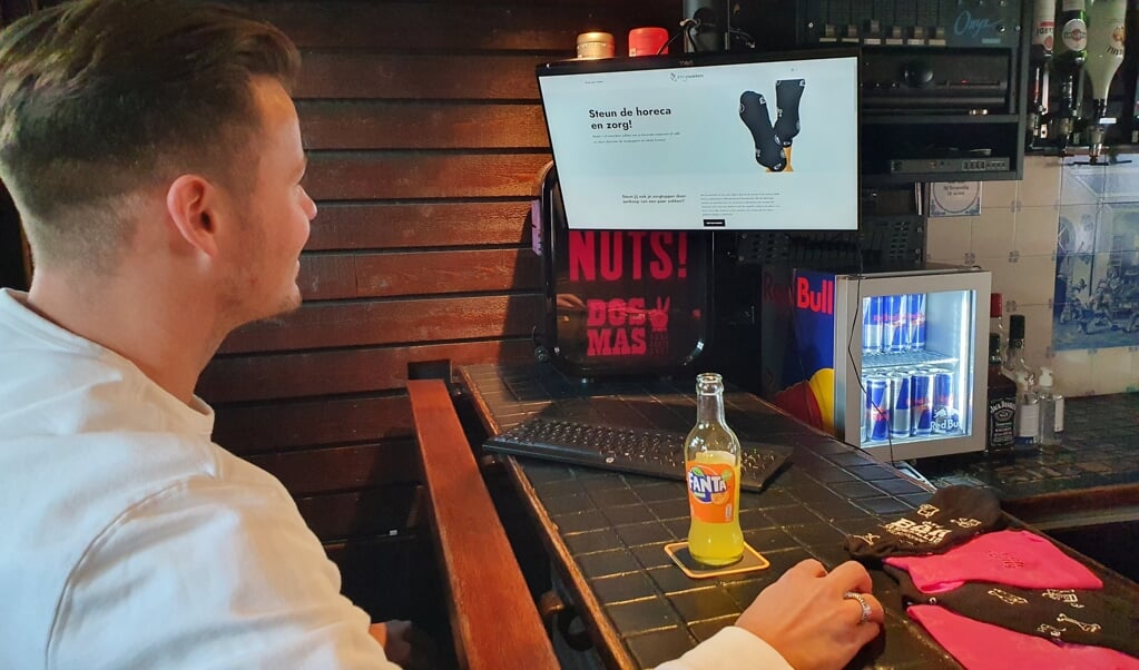Initiatiefnemer Gerard Vlastuin kijkt op de website van Zorgsokken aan de bar bij Bar Gezellig. 