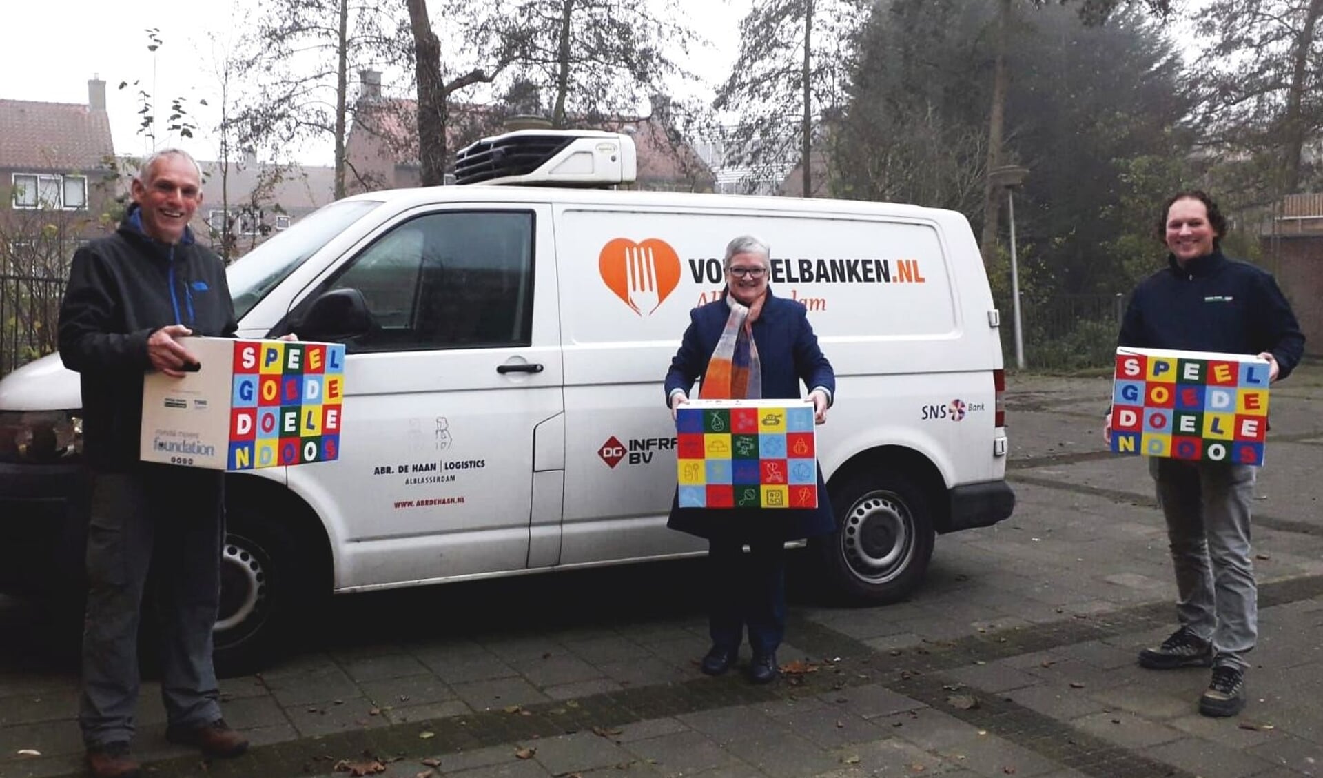 Ron van Zeggeren (bestuurslid Foundation) en Janco Romeijn (Mondial R. Vlot & Zn. Verhuizingen) overhandigen de Speelgoededoelendozen aan Anke van Veen van de Voedselbank. 