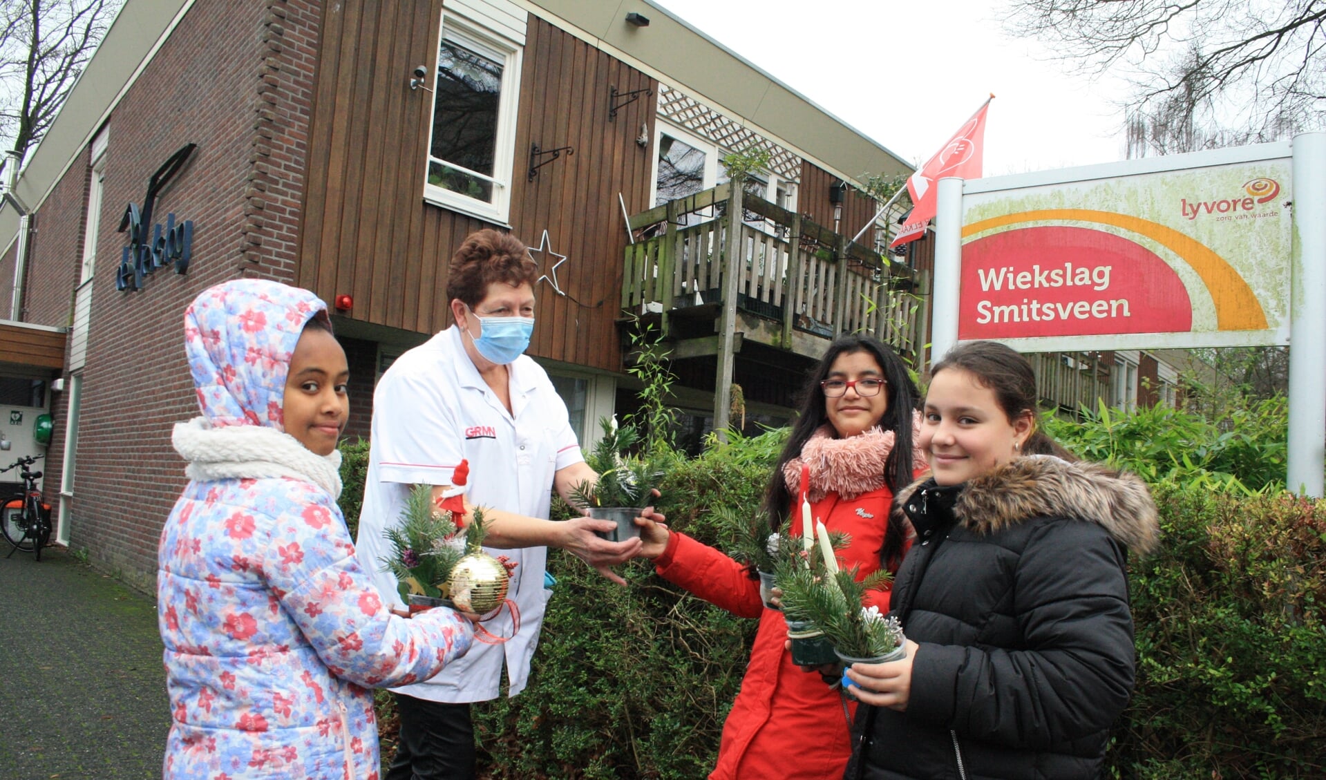Drie leerlingen uit groep 7 bieden kerststukjes aan bij verzorgingstehuis de Wiekslag.