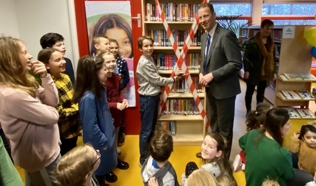 Voorleeskampioen Lucas en wethouder Berkhout knippen samen het lint door en openen daarmee de bibliotheek.