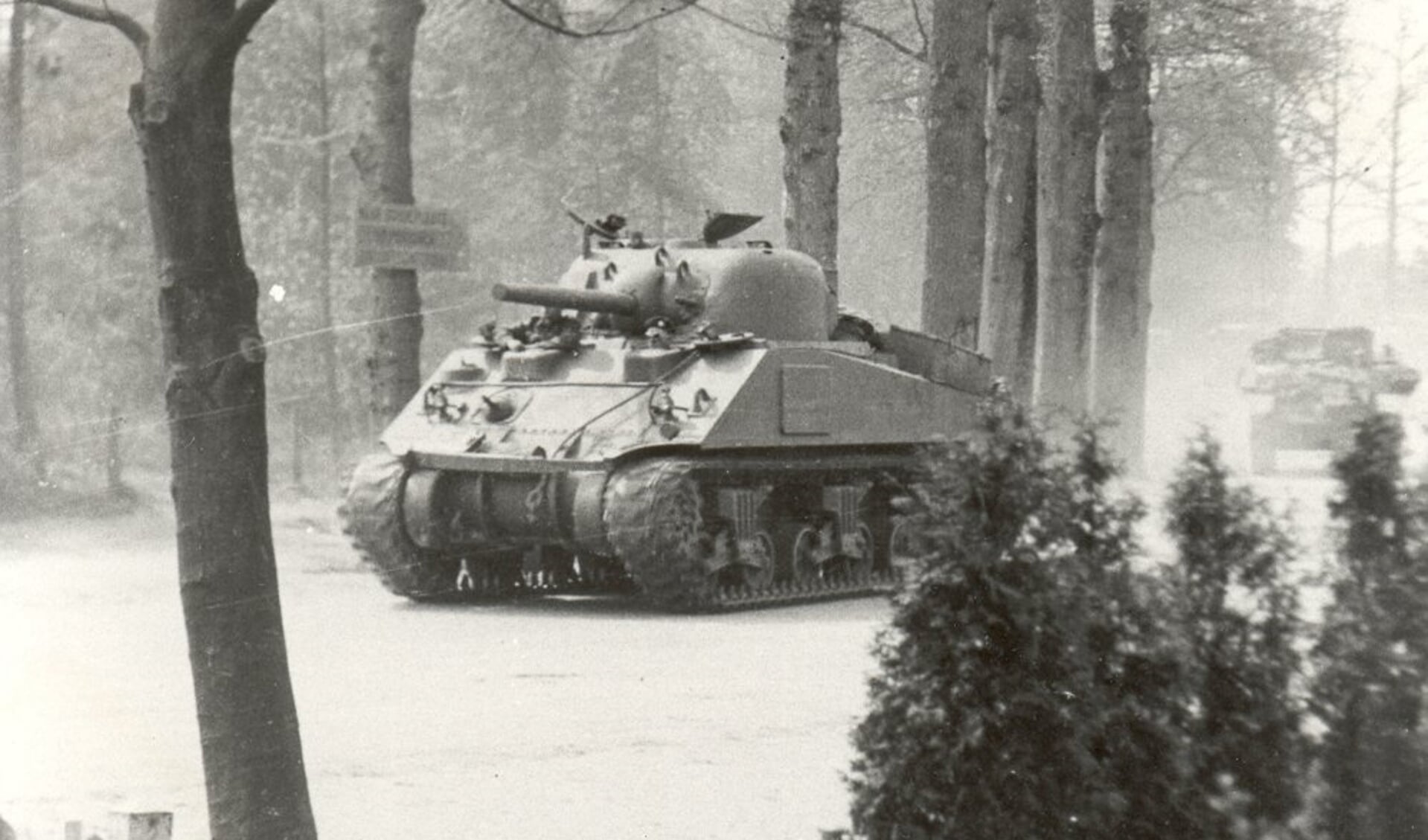 Een Canadese Sherman-tank rijdt vanuit de richting Apeldoorn het dorp Voorthuizen binnen. Links en rechts van de kanonloop zijn de hoofden van de chauffeur en een boordschutter zichtbaar.