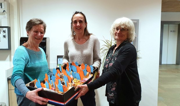 Nora Bakker (li) en Margaret Paige (re) bieden Mariëlle Versluis gebak aan als dank voor het gebruik van de keuken en kantine bij Kind & Co,