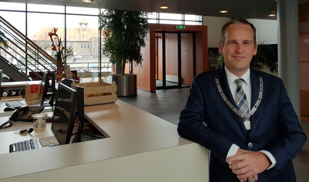 Bram van Hemmen in de hal van het gemeentekantoor met op de achtergrond het raadhuis waar hij de raadsvergaderingen voorzat.