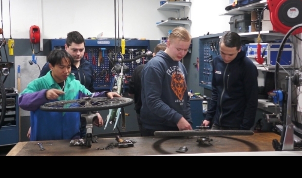 Stagiairs Art en Daan krijgen uitleg van fietsspecialist Denis (tweede van links) en zijn assistent Michael (geheel rechts) in de fietsenwinkel in Wageningen Noordwest.