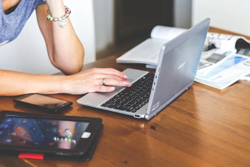 Een vrouw met een laptop, tablet en papier op tafel