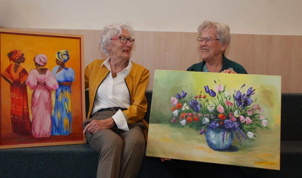 Ineke Bakker (links) en Joke Jansen met één van hun schilderijen die geëxposeerd worden in de bibliotheek.