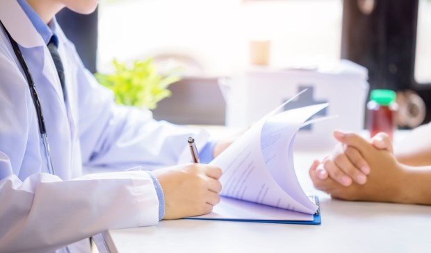 Doctor man consulting patient while filling up an application form at the desk in hospital. Medicine and health care concept