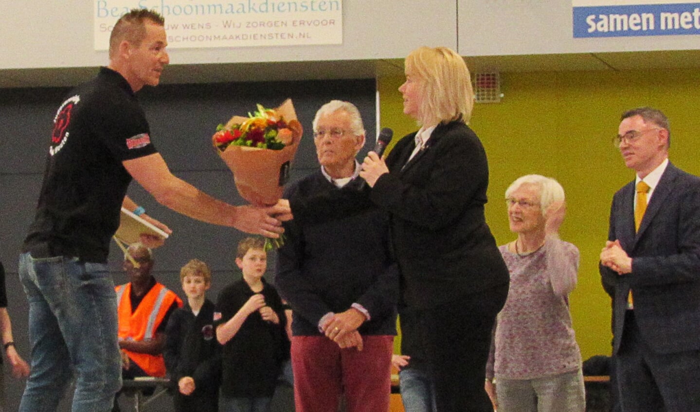 Ron van Lamoen krijgt uit handen van Jessica Boer een districtsonderscheiding  en bloemen uitgereikt.
