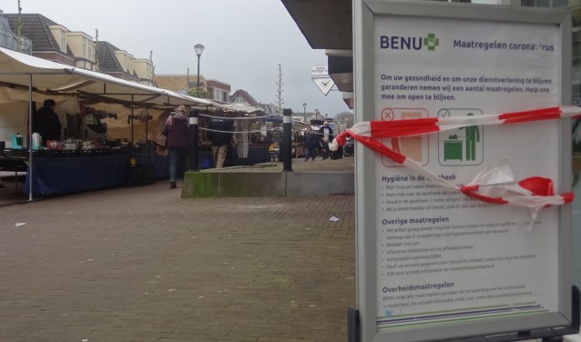 Een mededelingsbord met voorzorgsmaatregelen (en lint) bij de Benu Aportheek Soestdijk. Op de achtergrond draait de markt gewoon door.