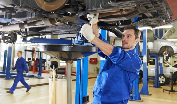 car mechanic with spanner tighten car suspension detail of lifted automobile at repair service station