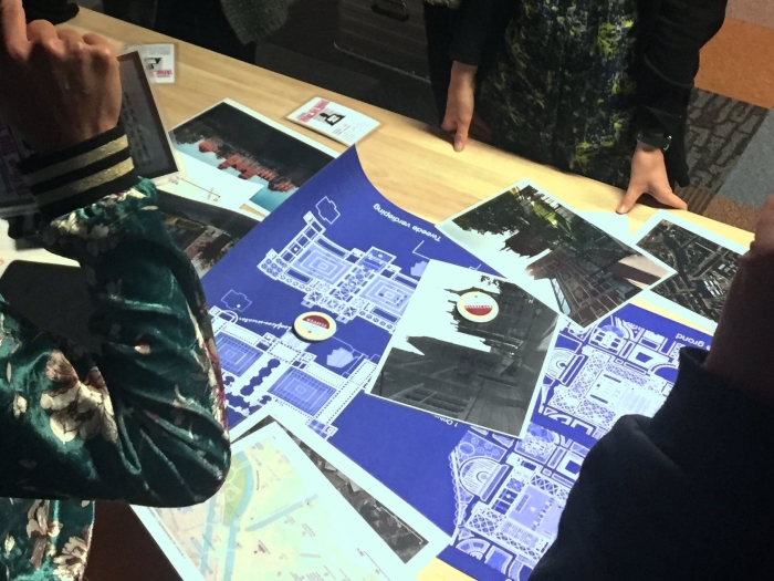Blueprint en vage foto's op een tafel, omringd door deels afgebeelde mensen