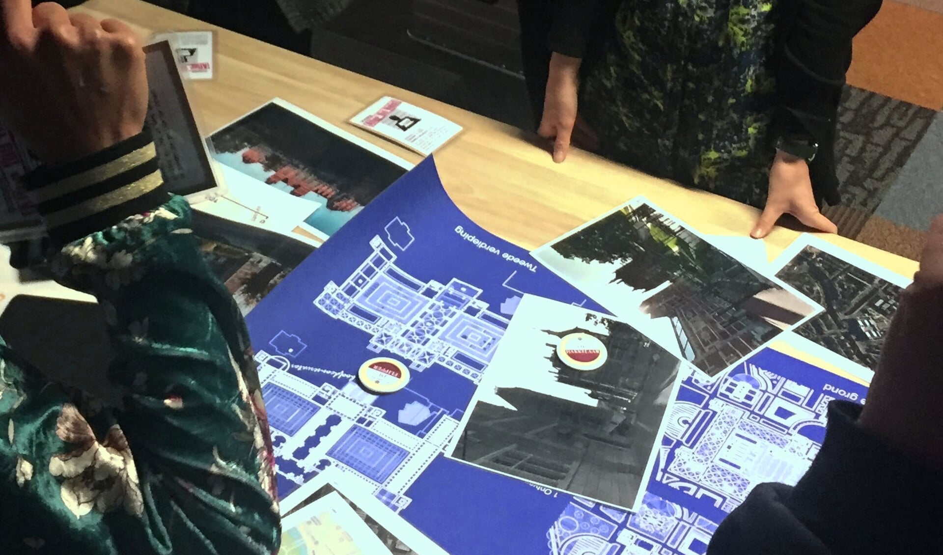 Blueprint en vage foto's op een tafel, omringd door deels afgebeelde mensen