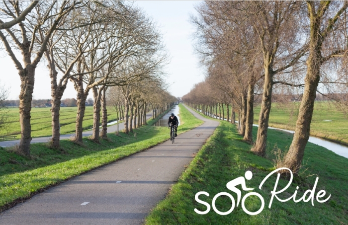 Fietser klimt dijk van de polder Purmer ten noorden van Amsterdam in Nederland op fietspad tussen boomlijnen