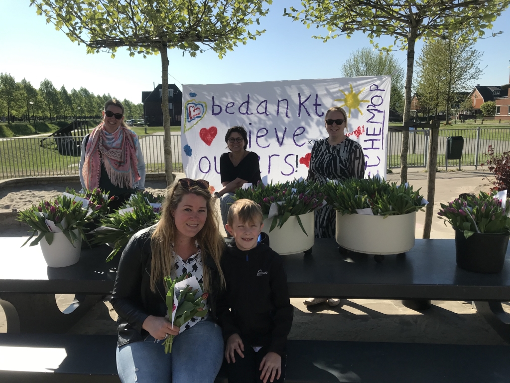 Ouder neemt samen met haar zoon de bloemen in ontvangst van de leerkrachten.